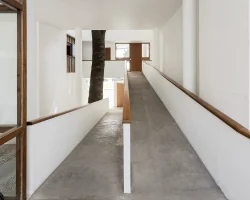 La rampa articula la residencia con el área profesional y organiza la circulación interior del conjunto. El recorrido ascendente genera perspectivas cambiantes y preserva el árbol preexistente en el patio.